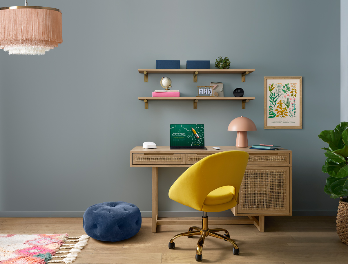 Una scrivania con sopra un computer, quadro, fogli e penna e l'Amazon eero 7, con la presa sotto alla scrivania che si intravede